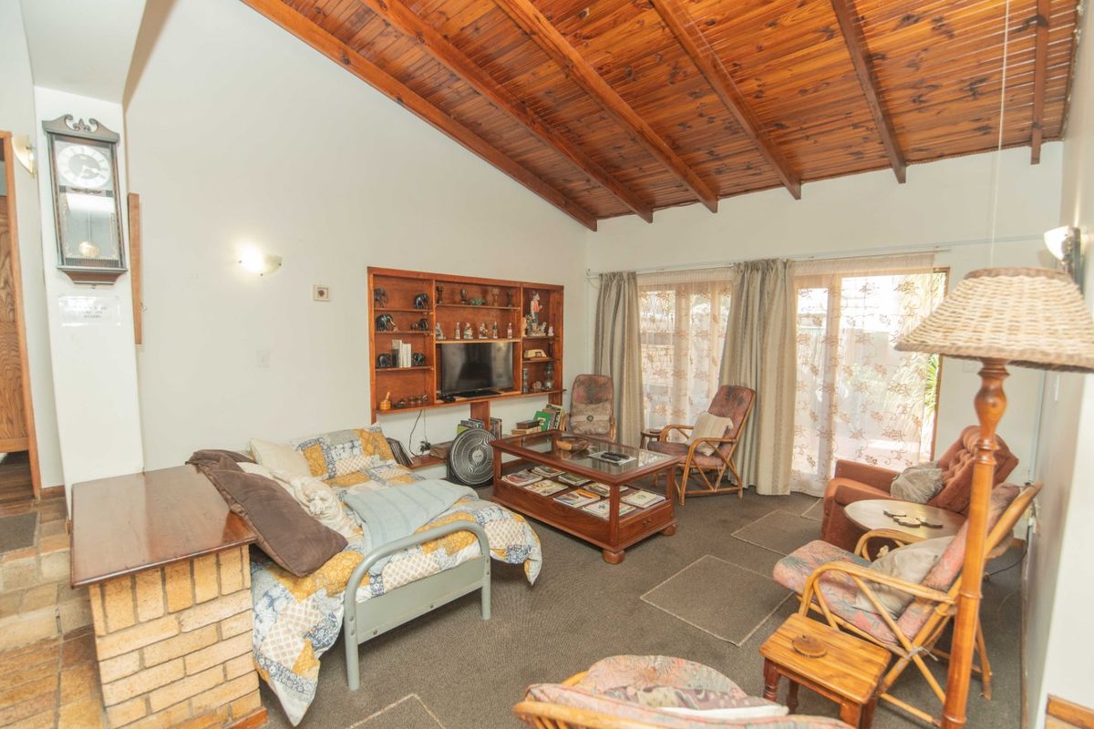 Living room featuring a high exposed timber beam ceiling, built-in shelving, a brick fireplace base, and sliding glass doors leading to the exterior.