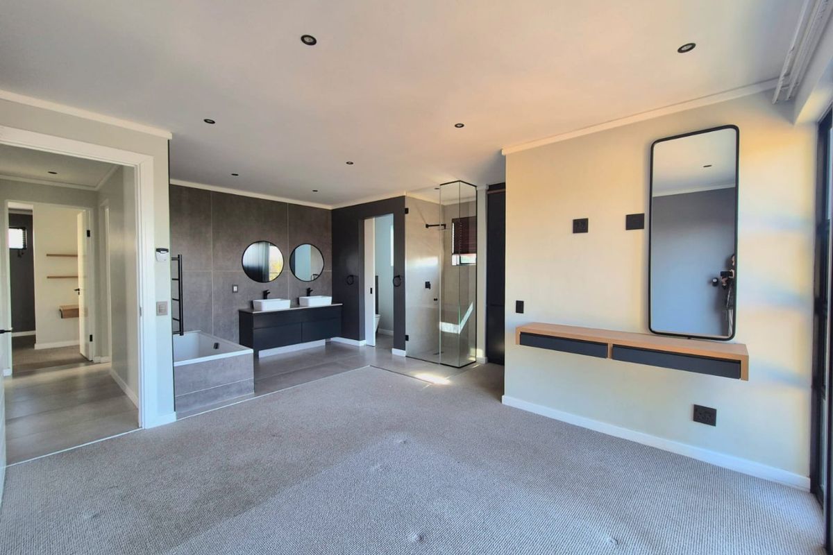Spacious bedroom featuring an integrated open-plan en-suite bathroom with a double vanity, built-in bathtub, and a modern glass-enclosed shower.