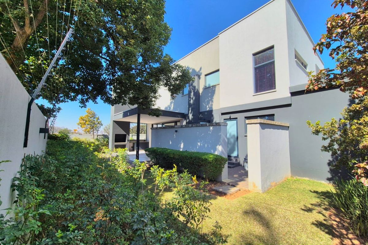 Rear view of the townhouse featuring a modern facade, a covered patio with a built-in braai, and a private garden area.