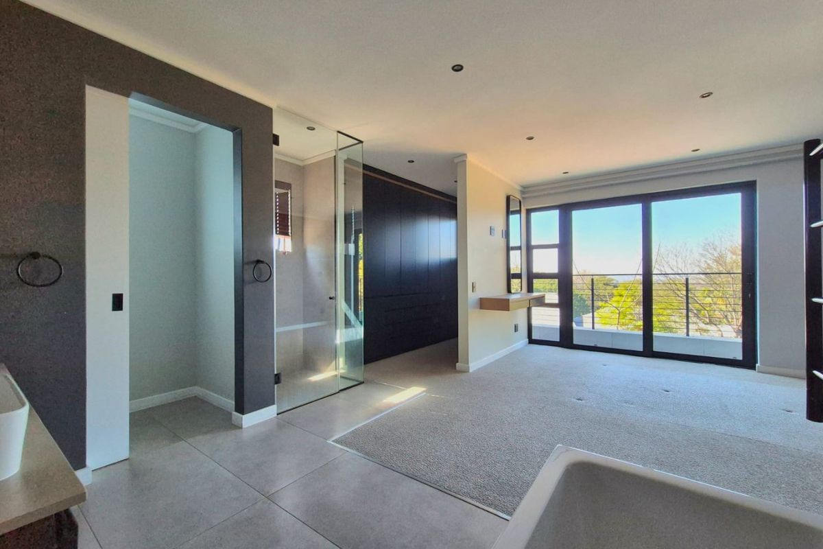 Spacious modern bedroom featuring built-in cabinetry, an en-suite glass shower, neutral carpeting, and large sliding doors opening to a private balcony.