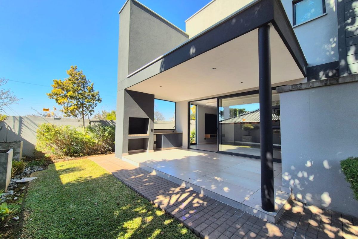 Modern covered patio featuring a built-in braai, outdoor cabinetry, and large sliding glass doors providing seamless indoor-outdoor flow to the garden.