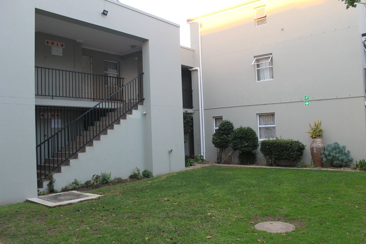A view of the apartment complex rear exterior, featuring a shared lawn area, metal staircase, and access to upper-level units.