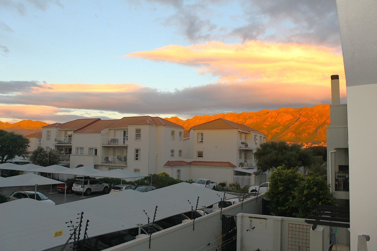 A scenic view of the apartment complex grounds featuring covered parking bays and a backdrop of sunset-lit mountains.