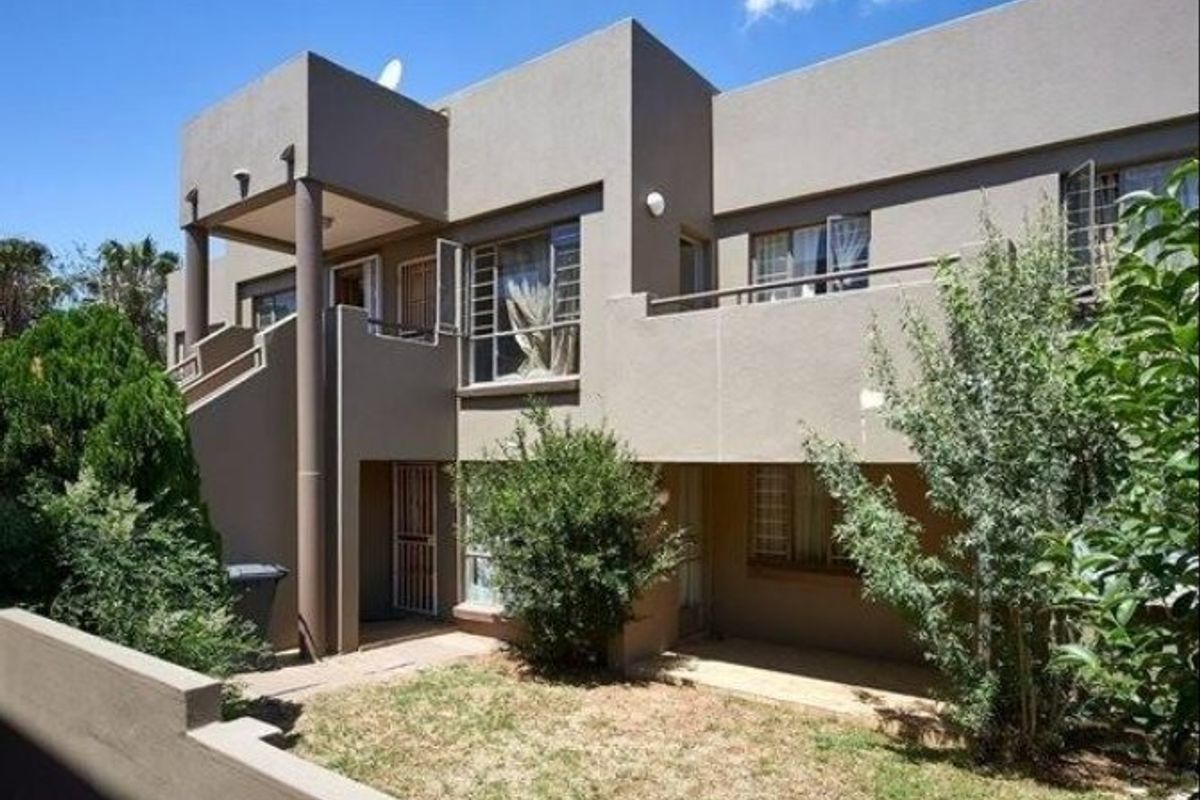 Rear view of a multi-story apartment building featuring a balcony, external staircase, and a small private garden area.