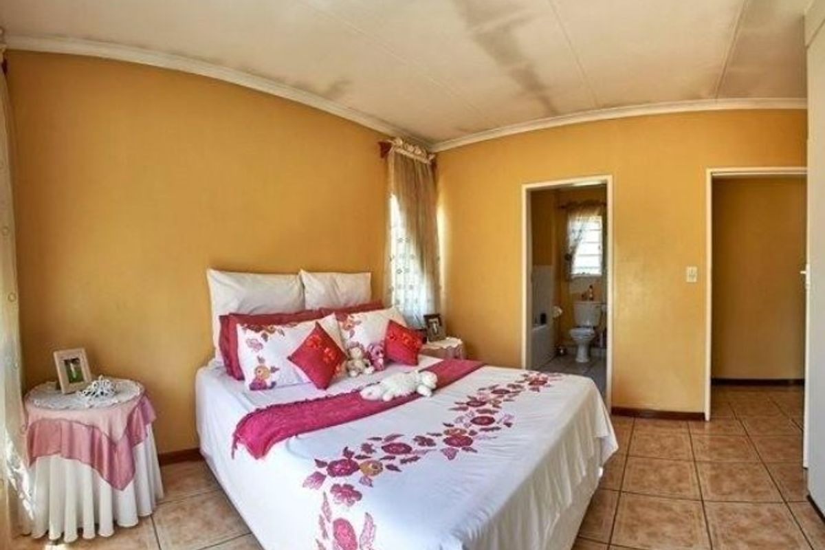 A bedroom featuring tiled flooring and an en-suite bathroom, showing signs of wear including ceiling water staining and dated wall finishes.