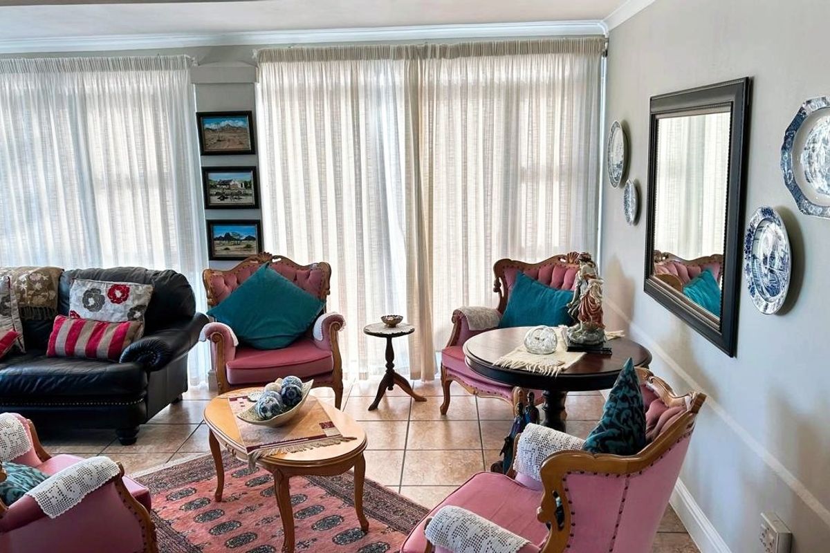 A comfortable living room featuring tiled flooring and large windows with floor-to-ceiling curtains, providing ample natural light.