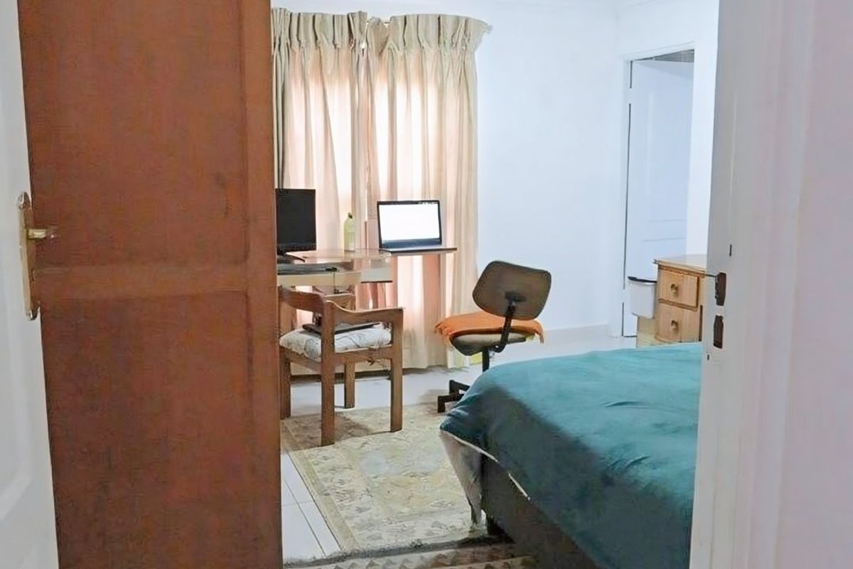 A view into a bedroom featuring neutral walls and flooring, currently utilized as a combined sleeping and workspace area.