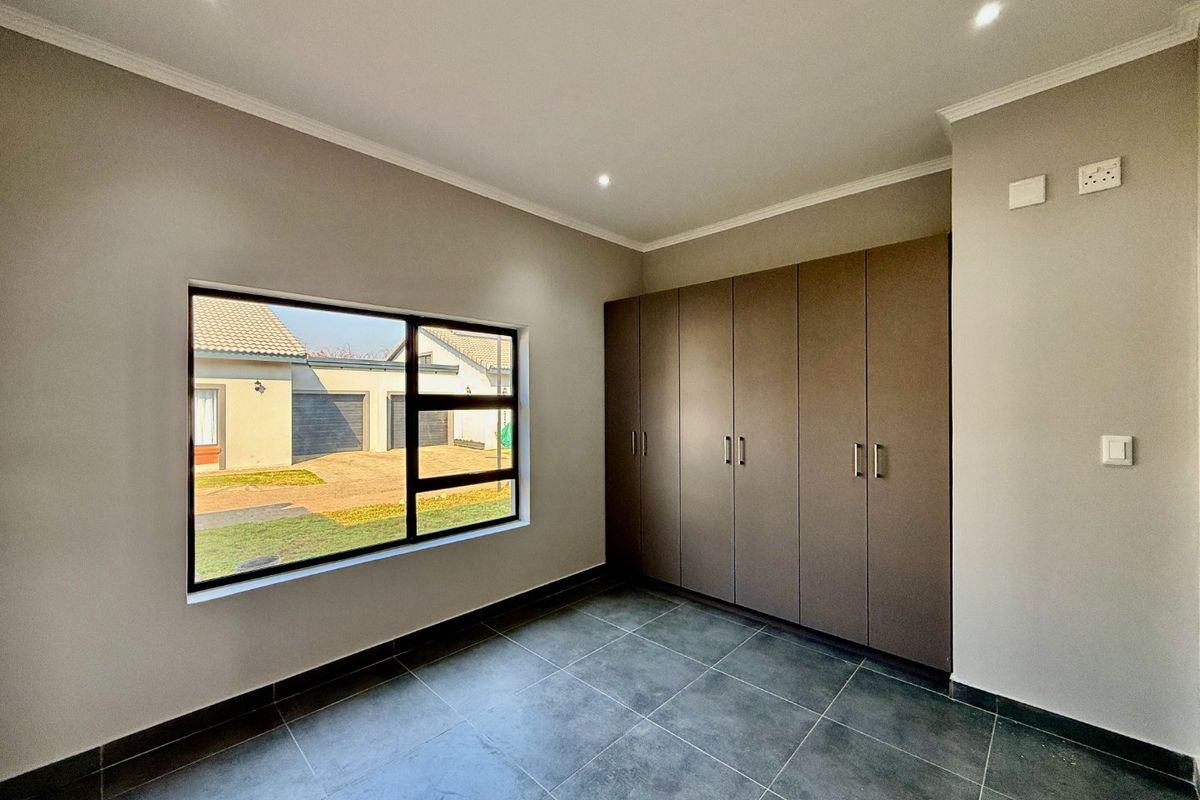 A clean, modern bedroom featuring neutral walls, dark tiled flooring, recessed lighting, and ample built-in cupboard storage.