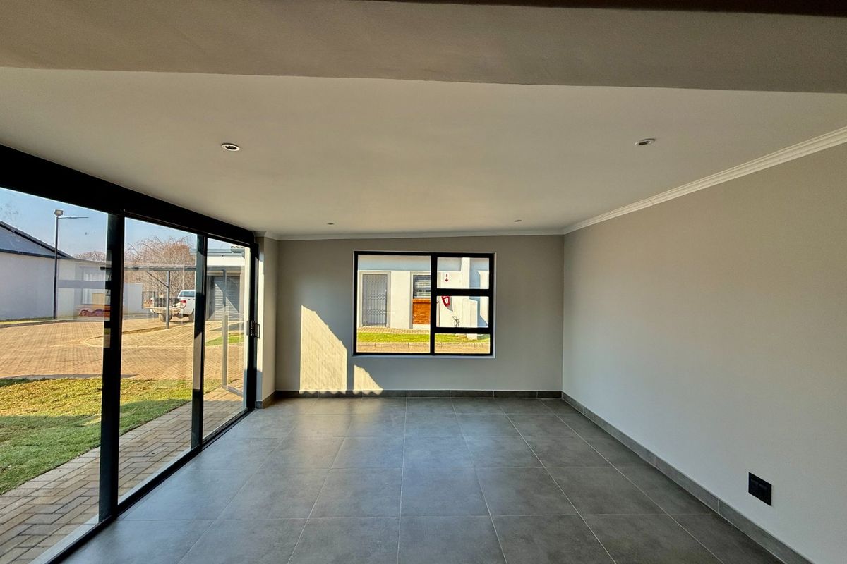 A bright, empty living area featuring large sliding glass doors, modern tiled flooring, and recessed downlights, offering a clean and neutral space.