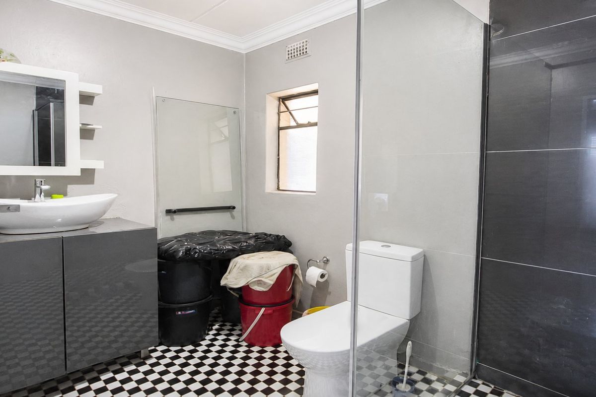 A modern bathroom featuring a vessel sink, vanity cabinet, glass shower enclosure, and distinctive black and white checkered floor tiles.