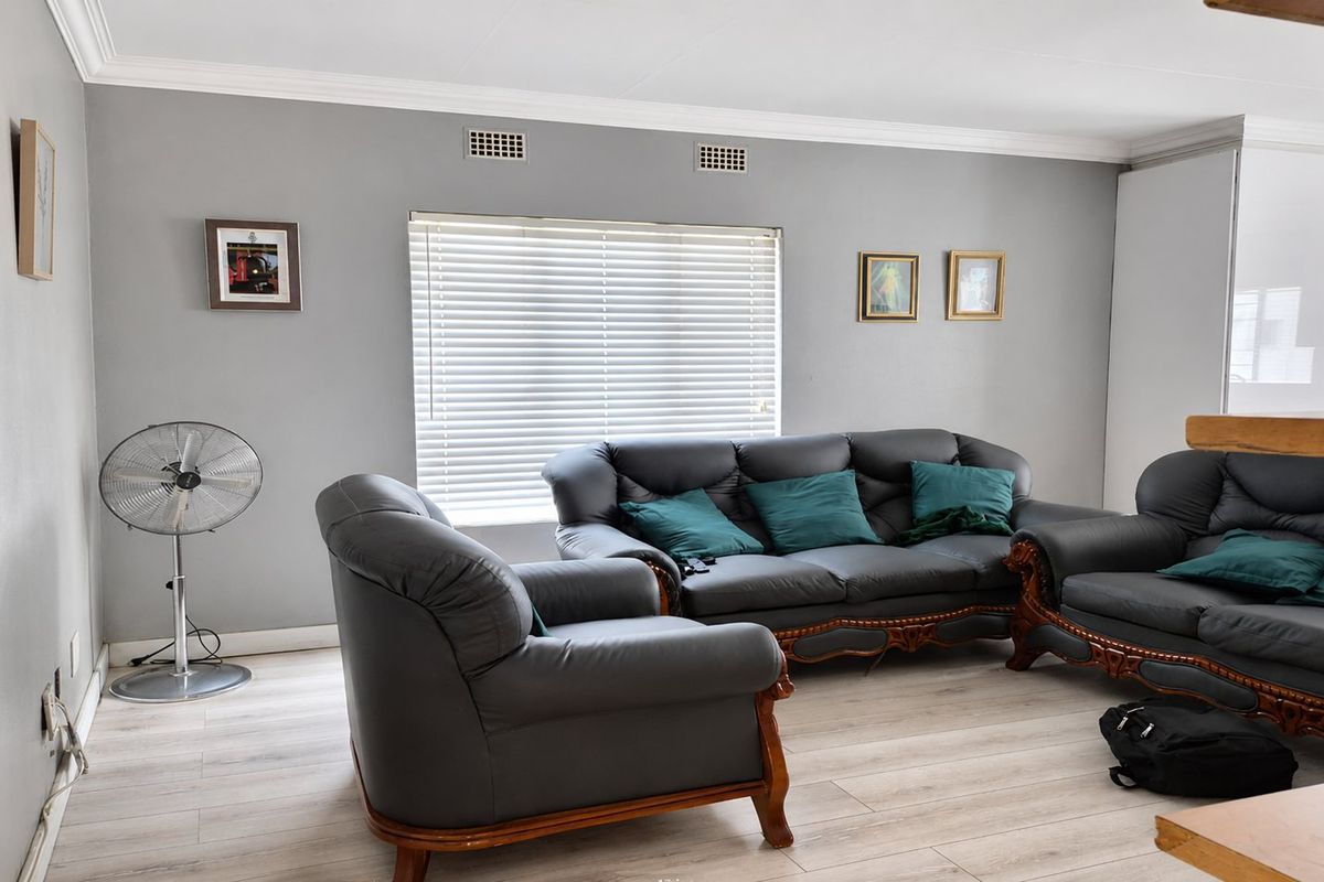 A well-lit living room featuring light-toned laminate flooring, crown molding, and venetian blinds, providing a neutral foundation for interior design.
