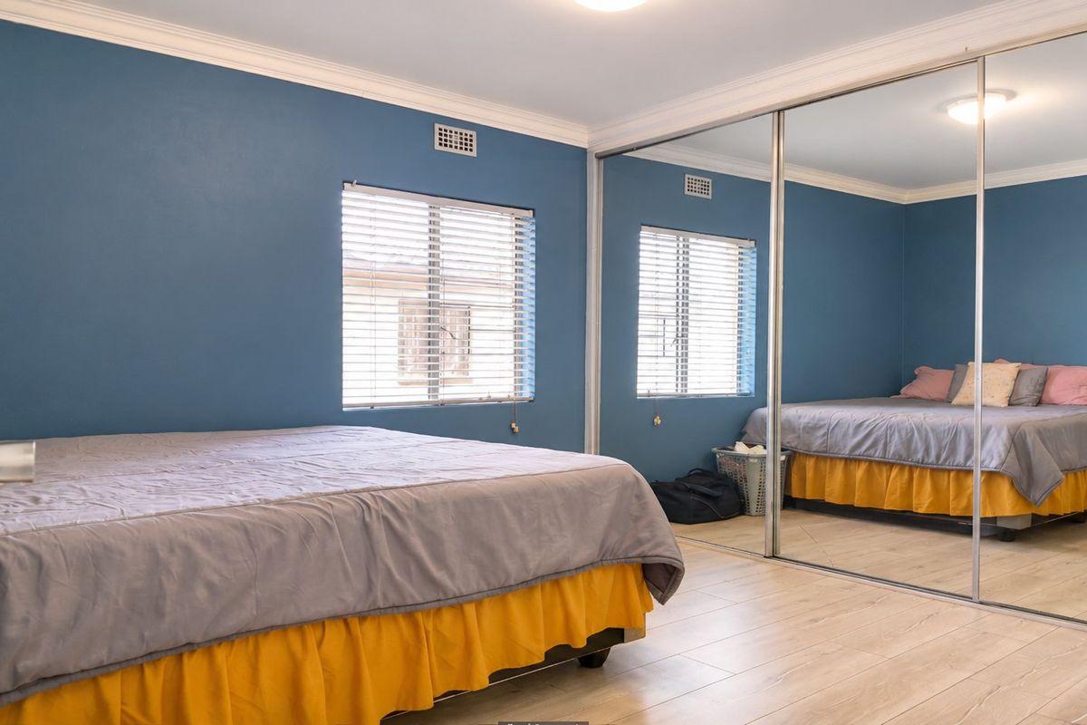 A well-maintained bedroom featuring laminate flooring, blue painted walls, and large mirrored sliding wardrobe doors that enhance the sense of space.
