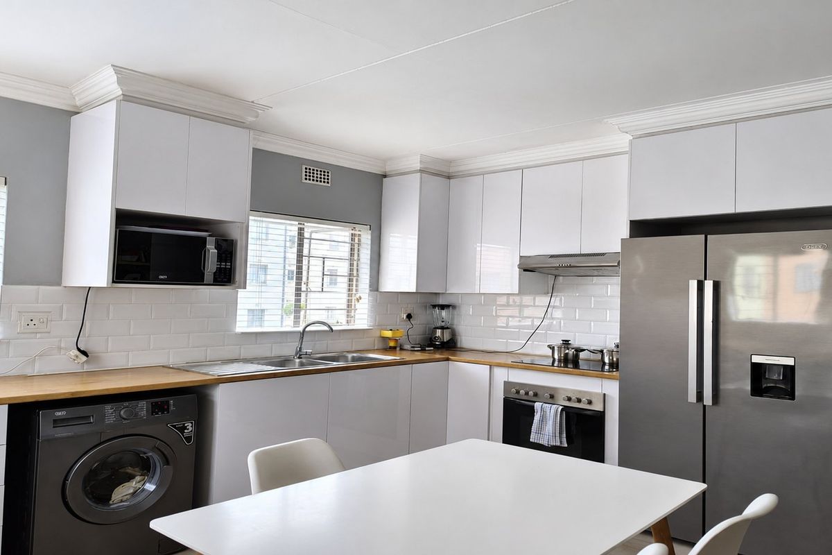 Modern kitchen featuring white gloss cabinetry, wooden countertops, subway tile backsplash, and integrated appliances including an oven, extractor fan, and washing machine.