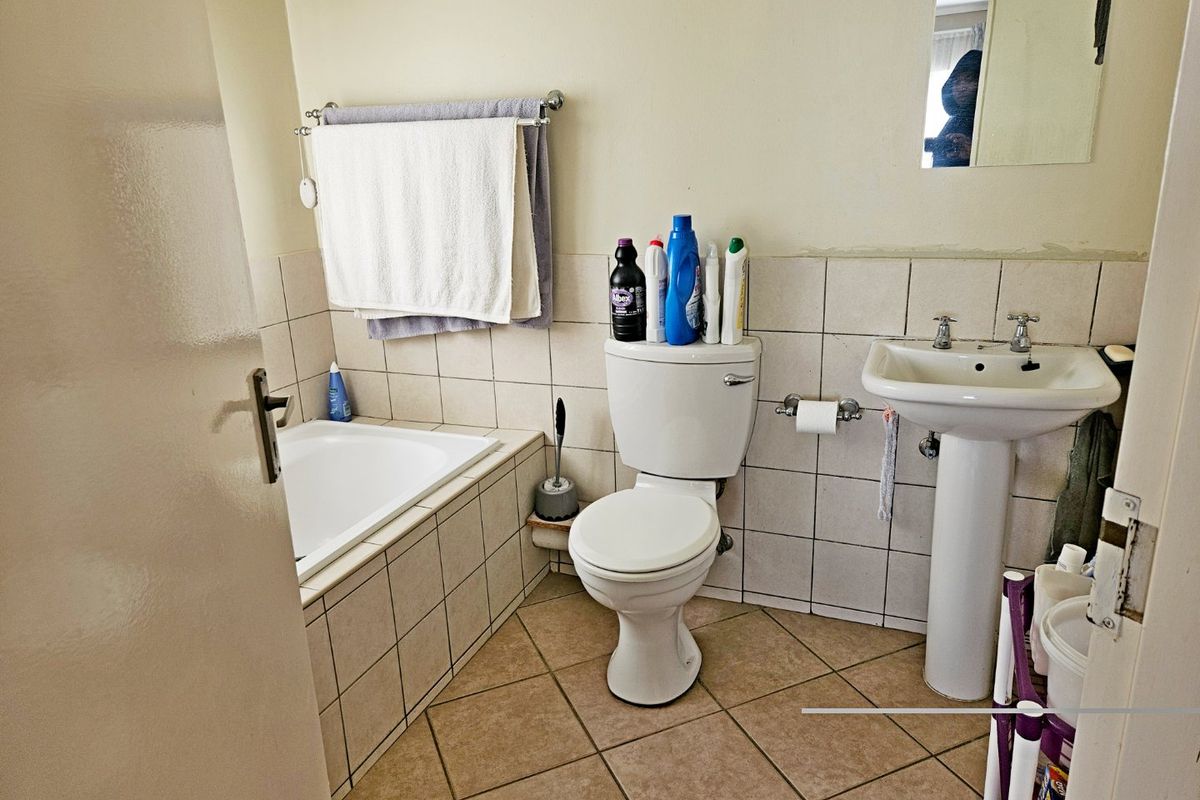 A functional bathroom featuring a pedestal basin, built-in bathtub, and tiled finishes, requiring minor cosmetic updates to improve its overall presentation.
