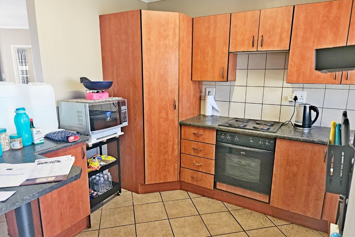 A functional kitchen featuring wood-finish cabinetry, laminate countertops, a built-in oven with electric hob, and tiled flooring.