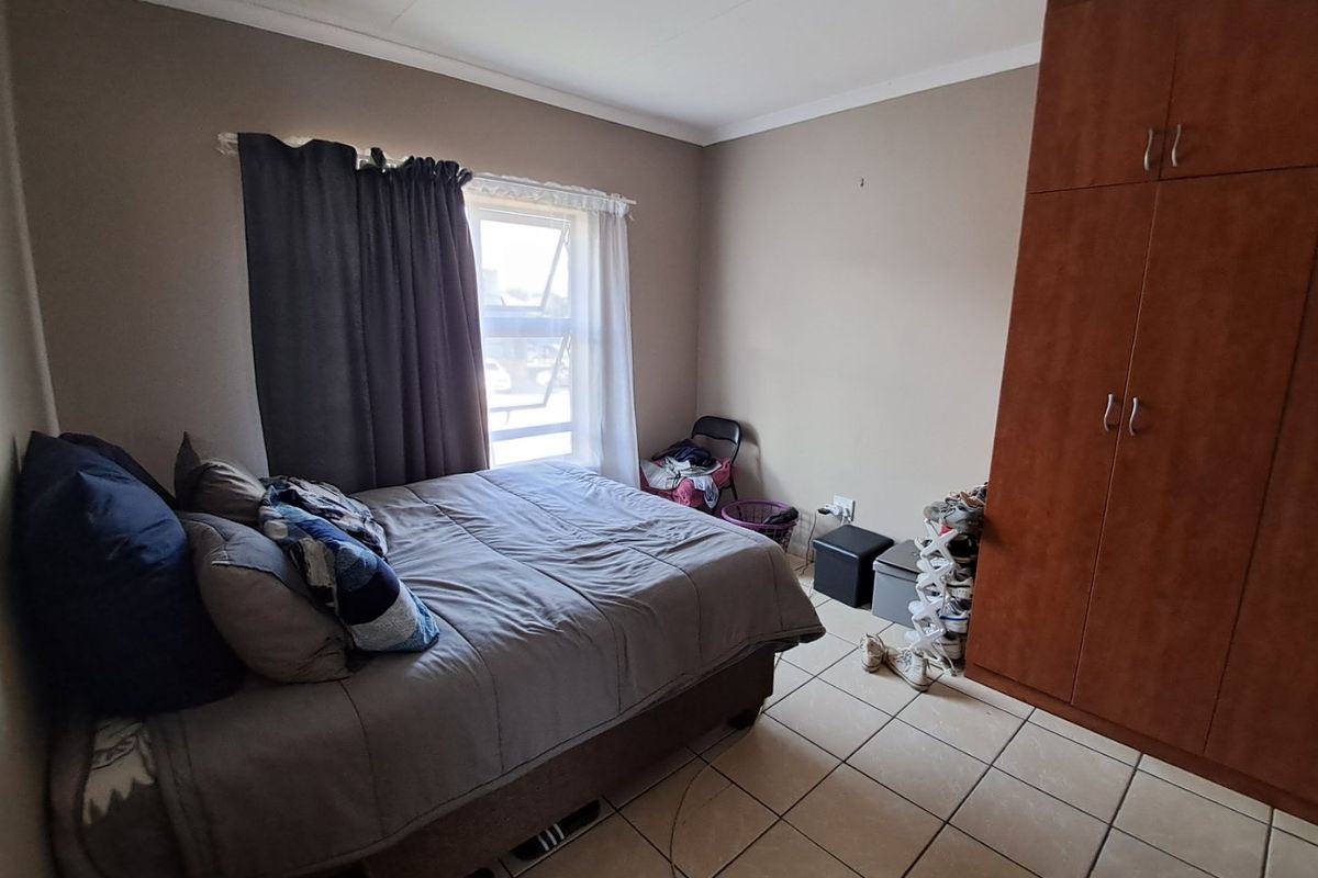 A functional bedroom featuring tiled flooring, a built-in wooden wardrobe, and a window with curtain treatments.