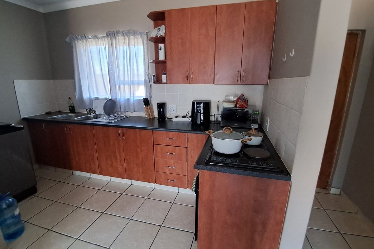 A functional kitchen featuring wood-look laminate cabinetry, dark countertops, ceramic tile flooring, and a built-in electric hob with tiled backsplash.