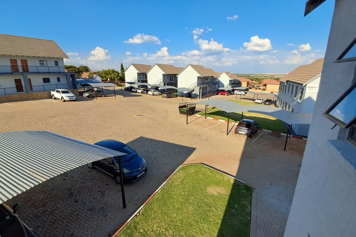 Elevated view of an apartment complex courtyard featuring paved parking bays, covered carports, and communal landscaped green spaces.