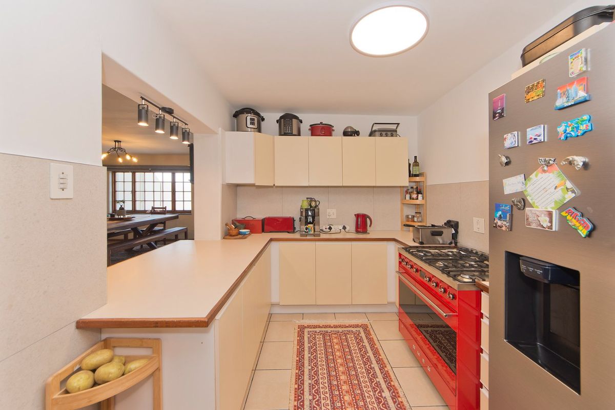 Functional kitchen featuring light-toned cabinetry, laminate countertops, and a prominent red gas range, with an open-plan layout connecting to the adjacent dining area.