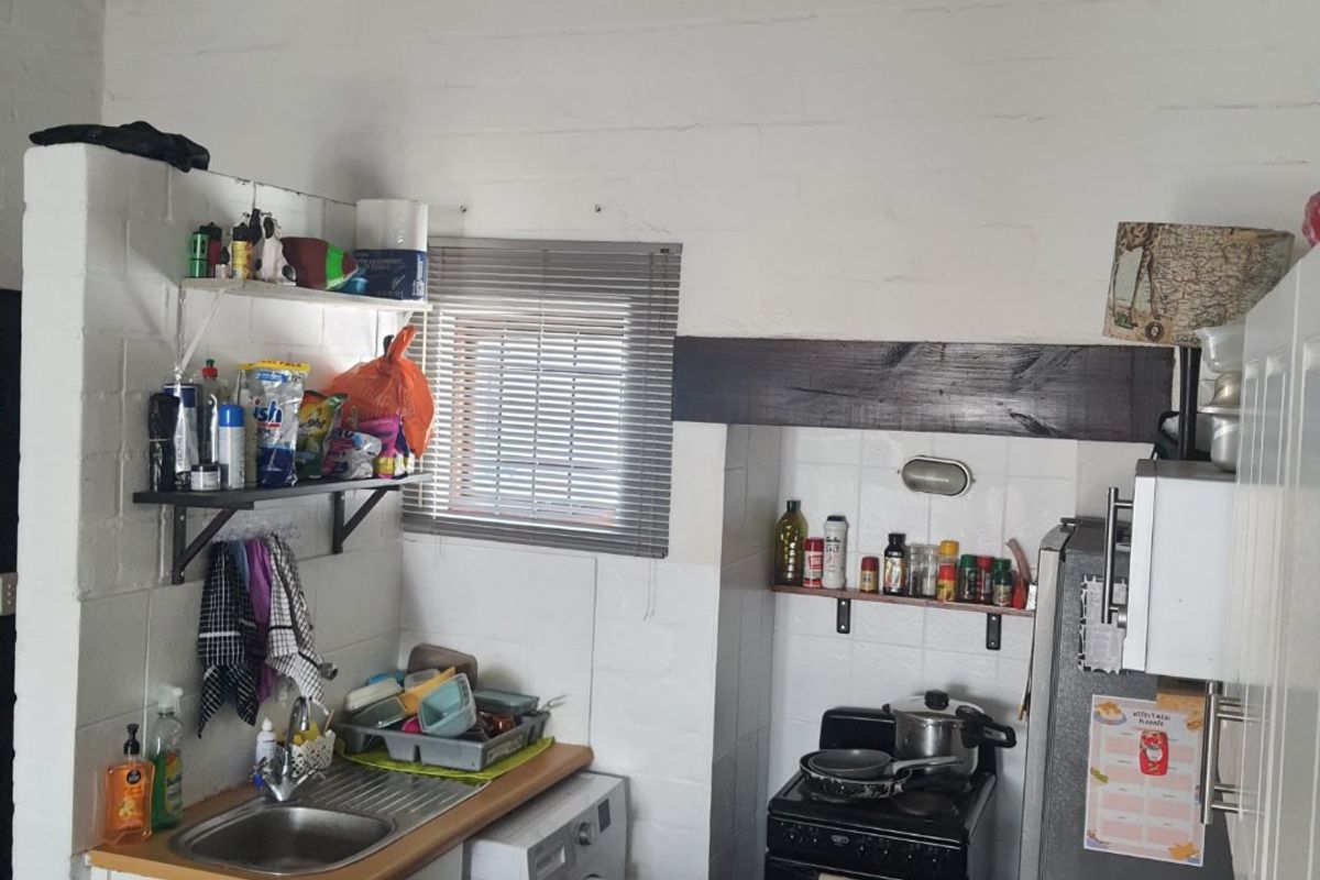 Compact kitchen featuring exposed timber beams, white painted brick walls, stainless steel sink, and built-in oven with tiled splashback.