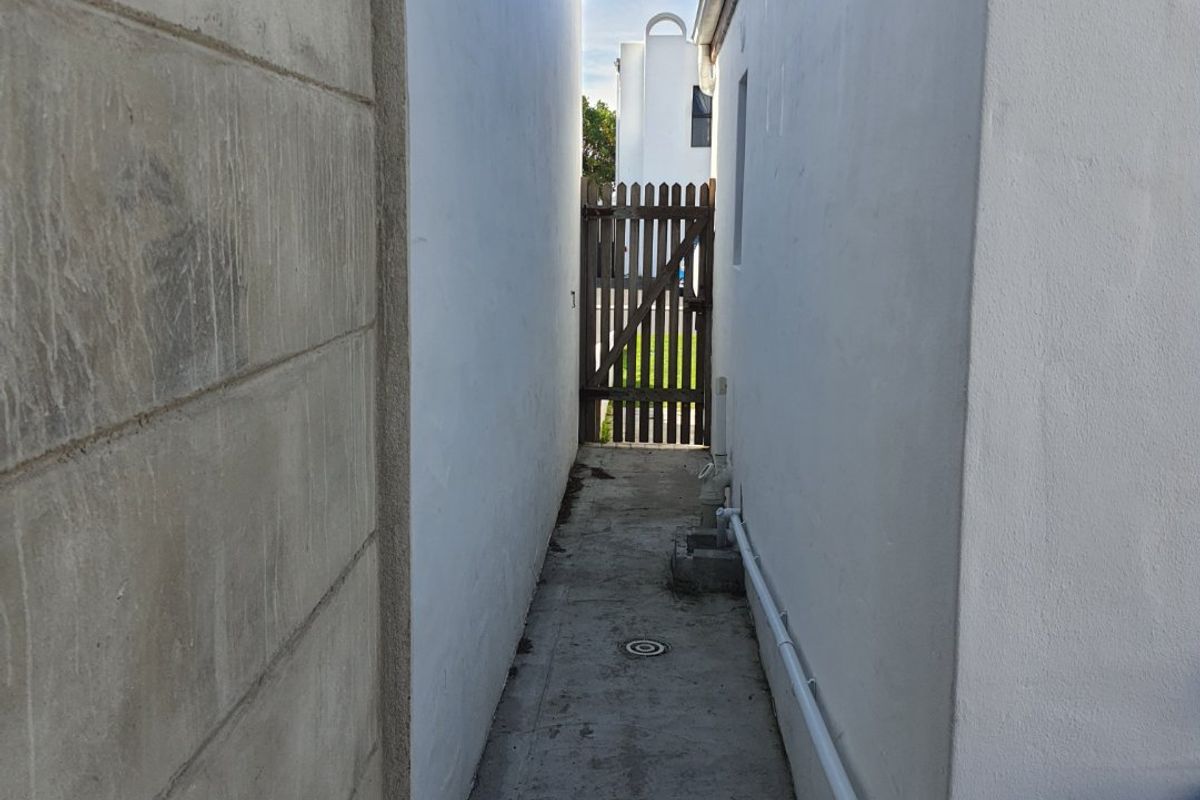 A narrow side passage between two exterior walls featuring a concrete pathway and a timber gate leading to the rear garden area.