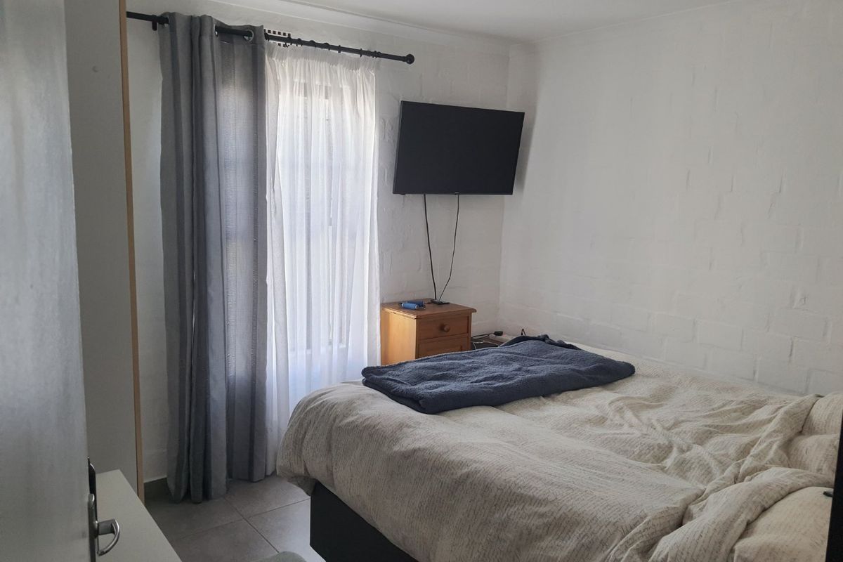 A functional bedroom featuring painted brick walls, tiled flooring, and a window with curtain fixtures.