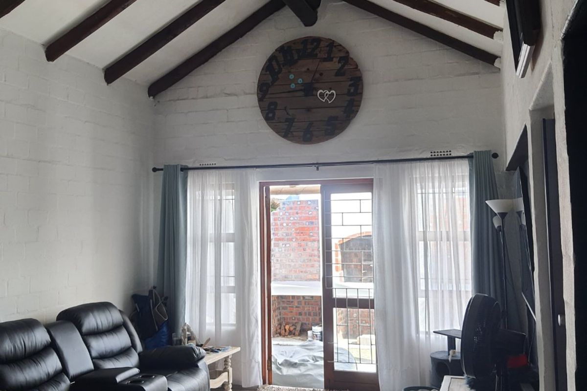 Living room featuring a vaulted ceiling with exposed timber beams, tiled flooring, and direct access to an outdoor area through a glass panel door.