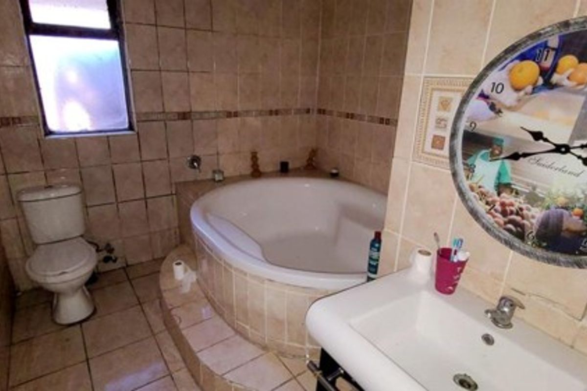 A functional bathroom featuring a built-in corner bathtub, pedestal washbasin, and toilet, finished with neutral ceramic wall and floor tiles.