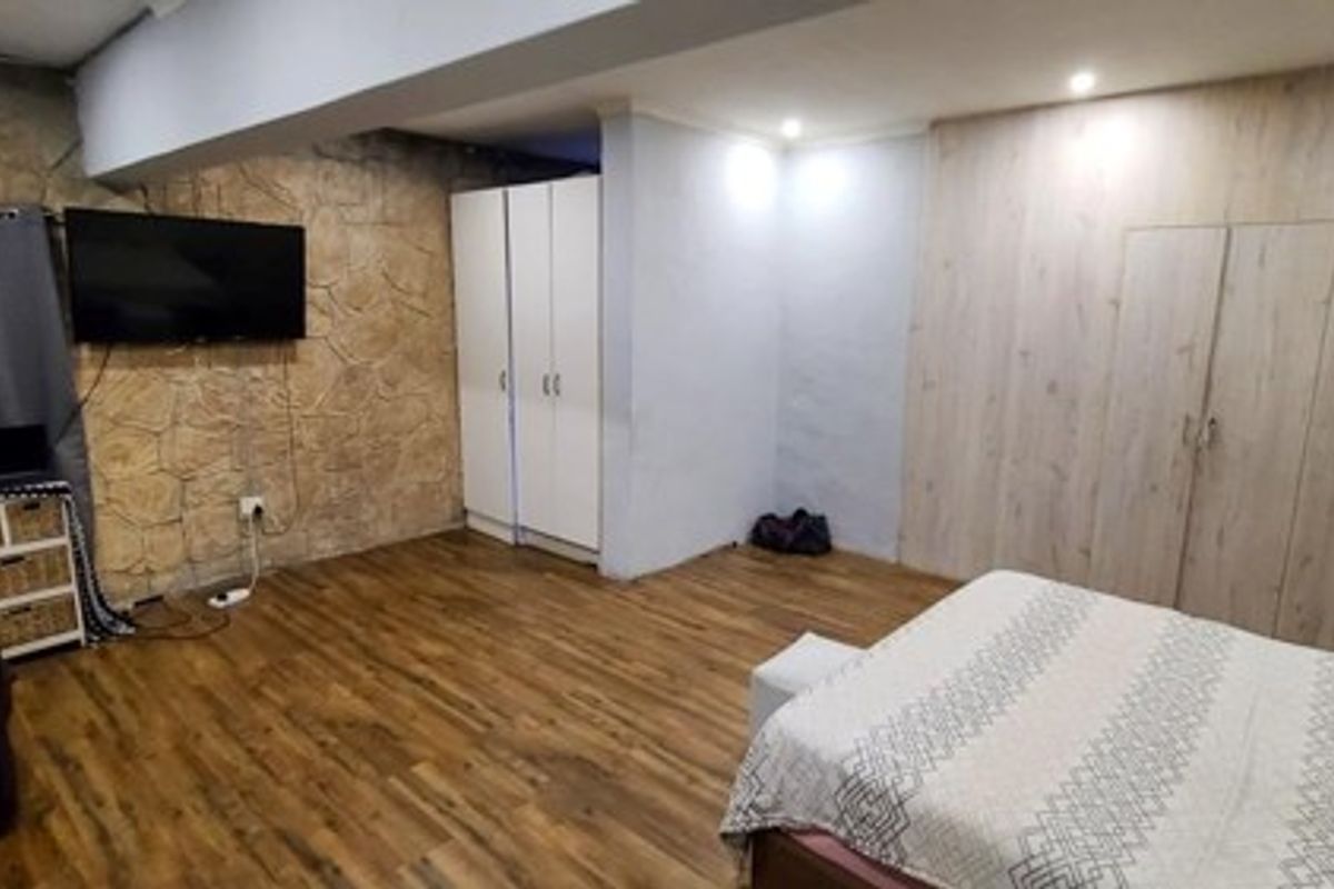 Spacious bedroom featuring laminate flooring, a textured stone feature wall, and extensive built-in cupboard storage with recessed lighting.