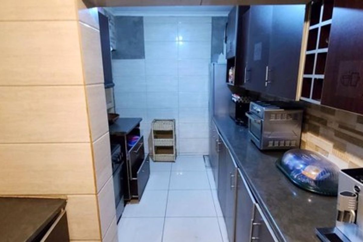 A functional kitchen featuring dark wood cabinetry, stone countertops, and tiled finishes, offering a practical layout with ample storage space.