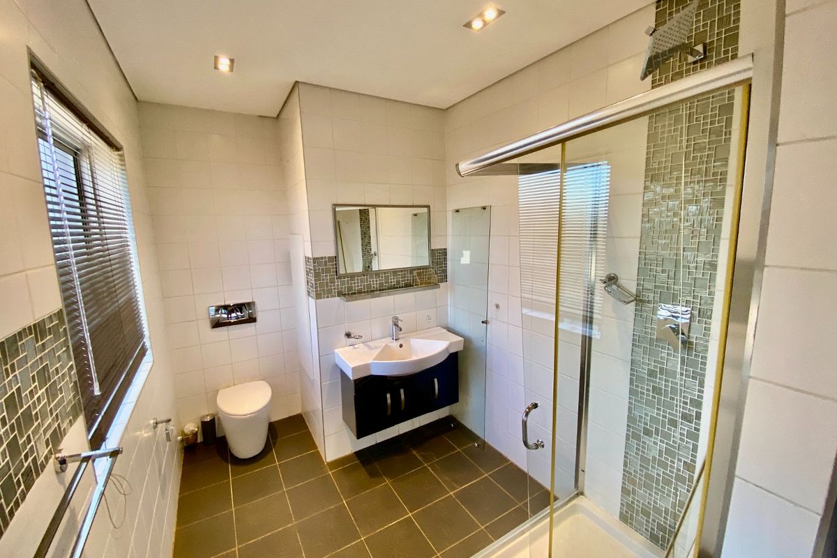 A clean, modern bathroom featuring a glass shower enclosure, wall-hung toilet, vanity unit, and decorative mosaic tile detailing.