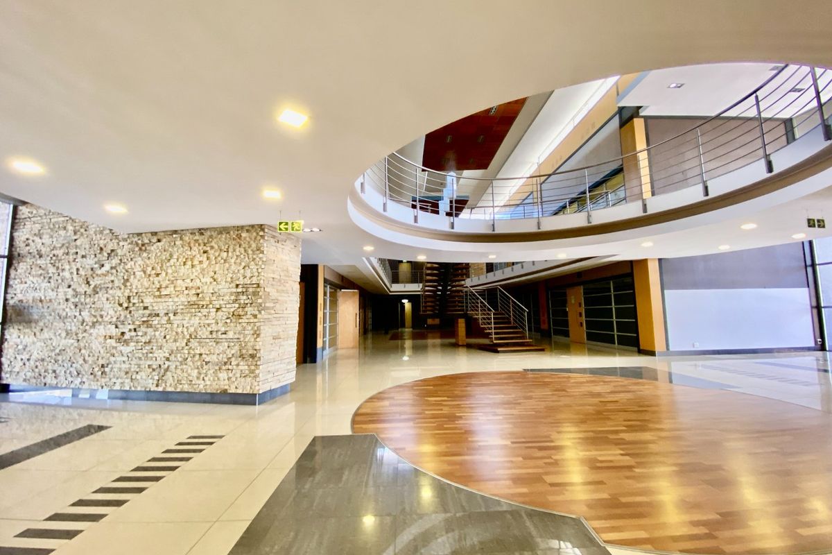 Spacious commercial atrium featuring a stone-clad feature wall, polished tile and timber flooring, and a mezzanine level with stainless steel balustrades.