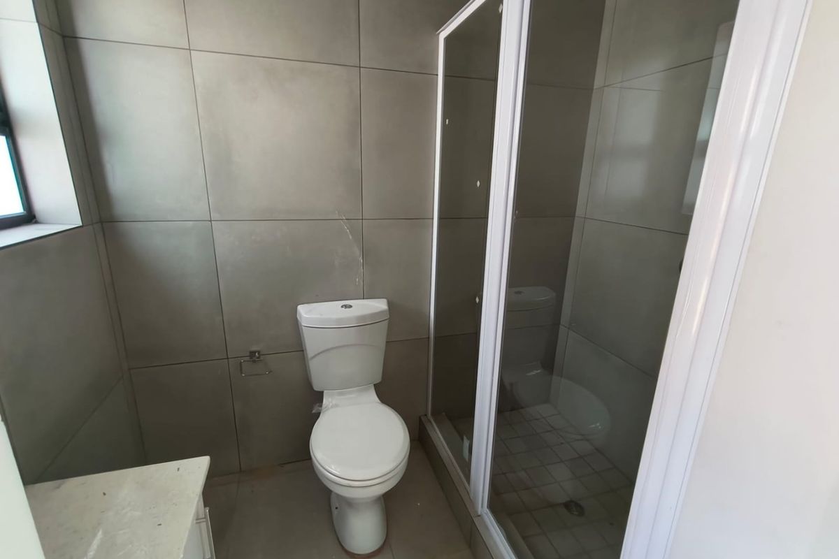 A functional bathroom featuring a shower enclosure, toilet, and vanity with neutral grey wall tiling.