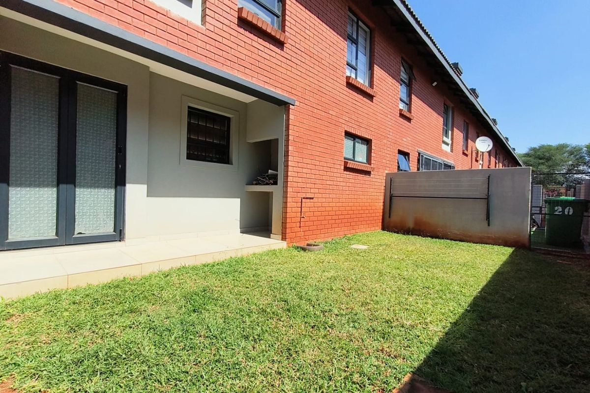 Rear exterior view of the townhouse featuring a private garden, tiled patio area with a built-in braai, and red brick facade.