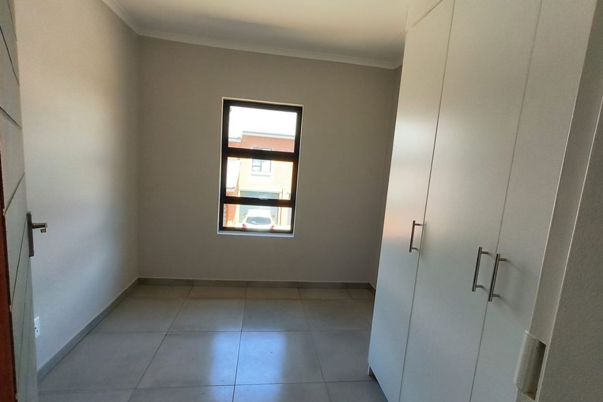 A clean, empty bedroom featuring neutral tiled flooring, built-in cupboards, and a modern aluminium window frame, offering a blank canvas for personalization.