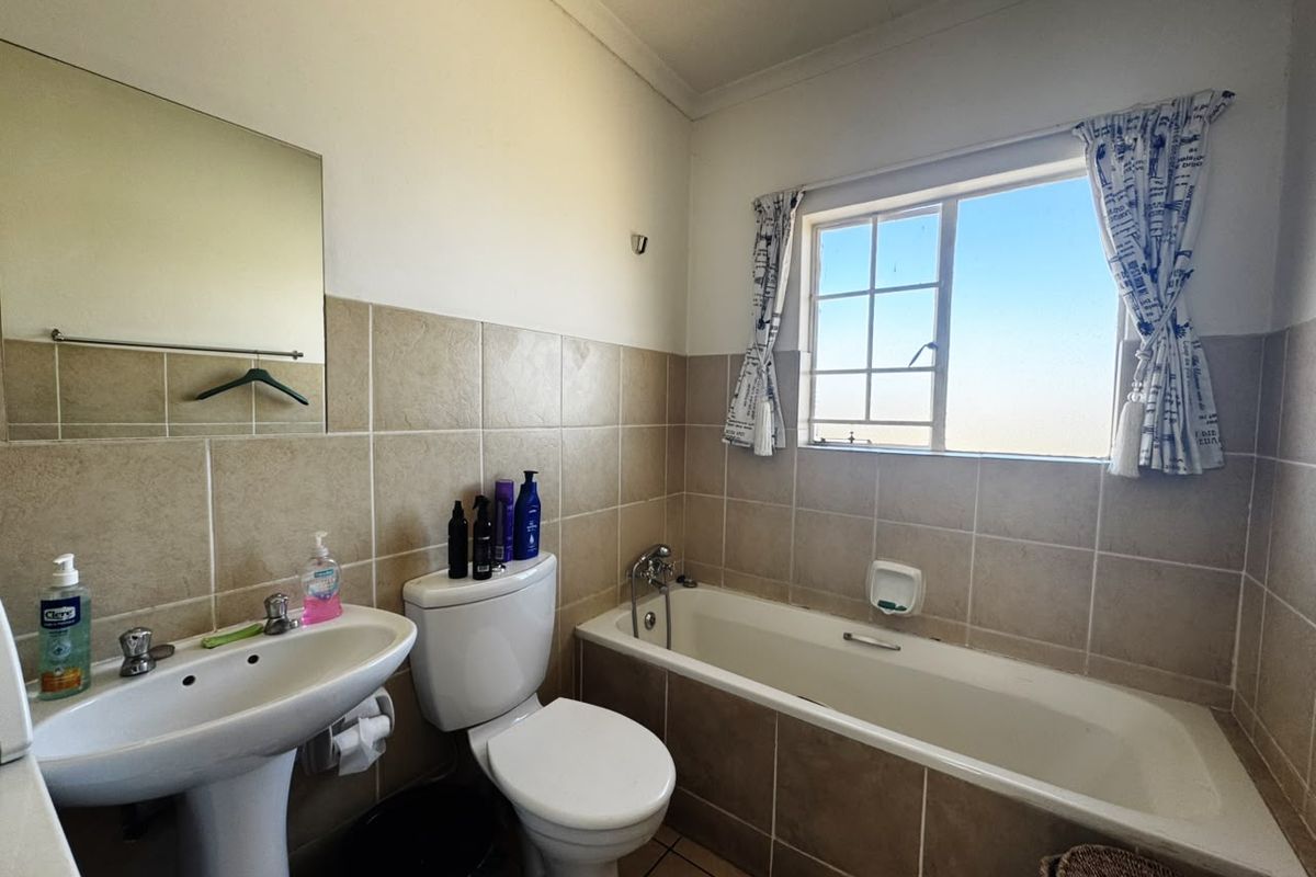 A functional bathroom featuring a pedestal basin, toilet, and a built-in bathtub with neutral wall and floor tiling.