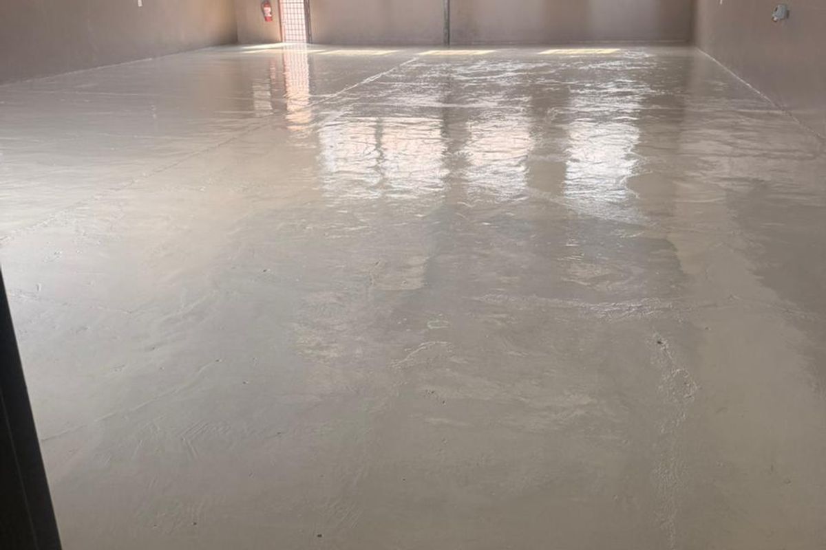 Spacious industrial warehouse unit featuring a clean epoxy-coated concrete floor, exposed steel roof structure, and natural light through security-barred windows.