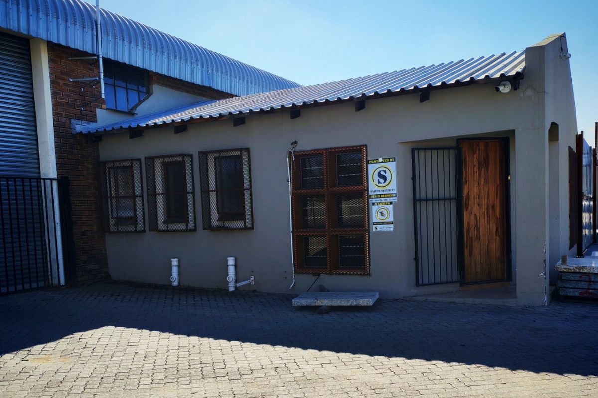 Front exterior view of an industrial property featuring a paved driveway, security-enhanced windows and doors, and a corrugated metal roof structure.