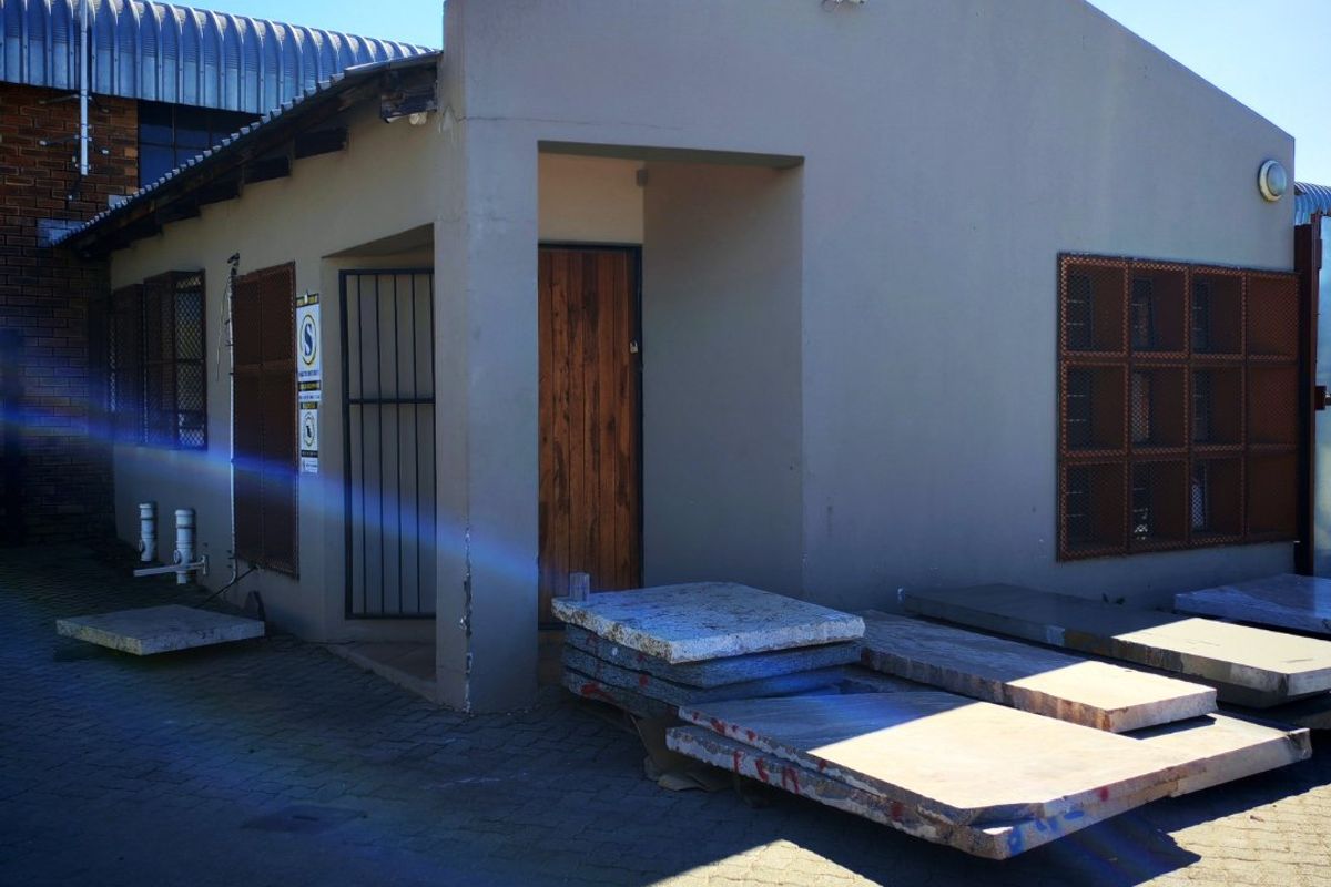 Exterior view of an industrial building featuring a paved entrance area, security gates, and protective window bars.