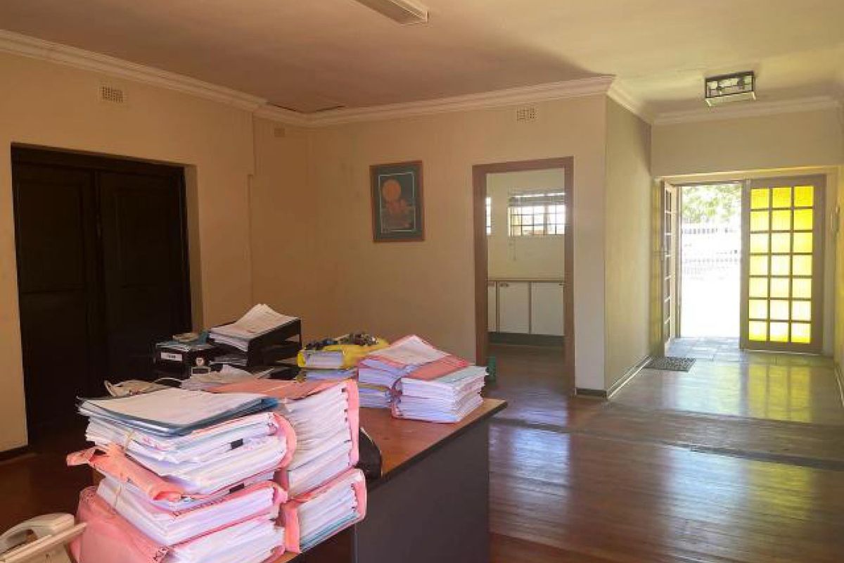 Spacious living area featuring hardwood flooring, decorative cornices, and access to an adjoining room and exterior entrance.