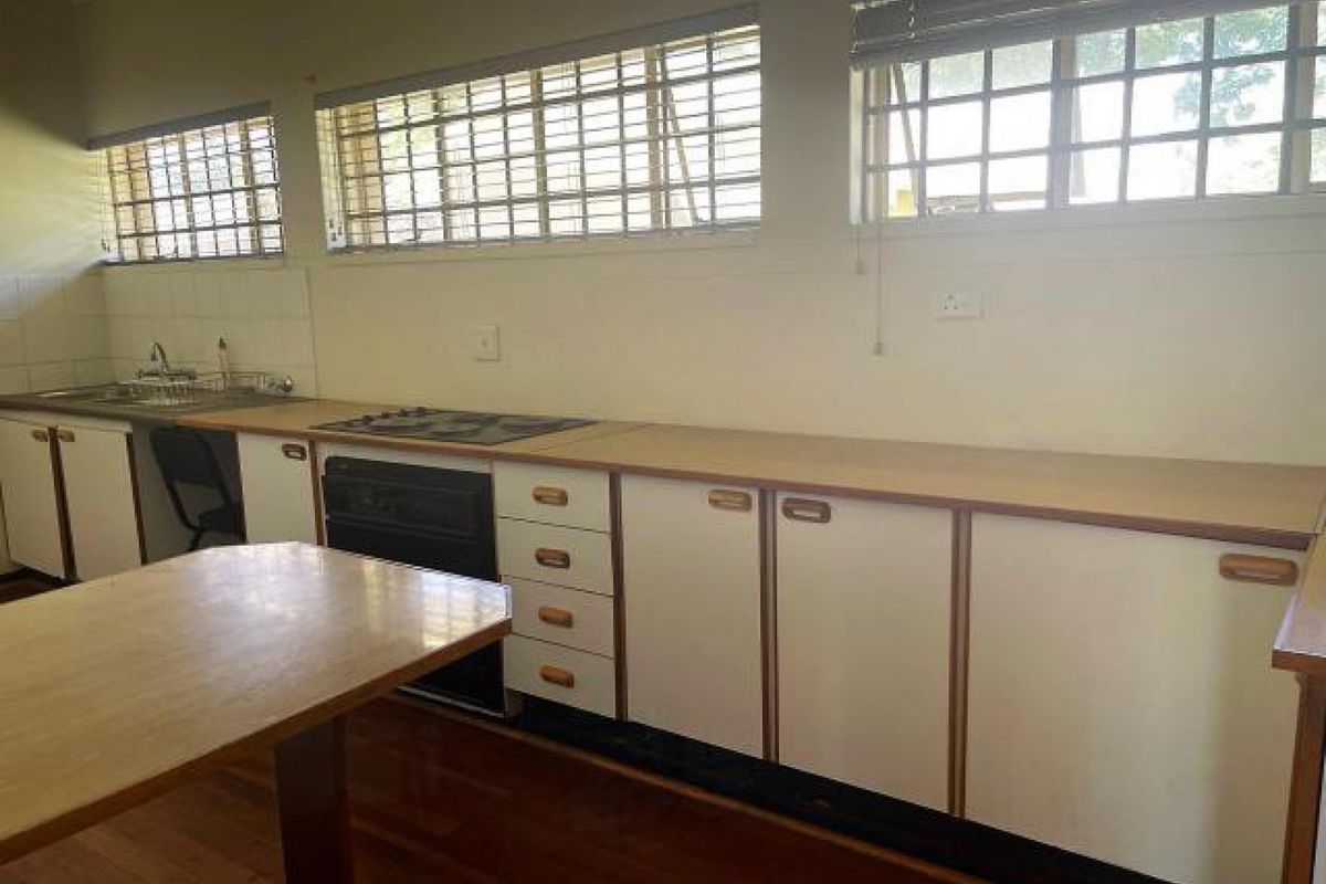 A functional kitchen featuring dated cabinetry, laminate countertops, a built-in oven and hob, and large windows with security bars.