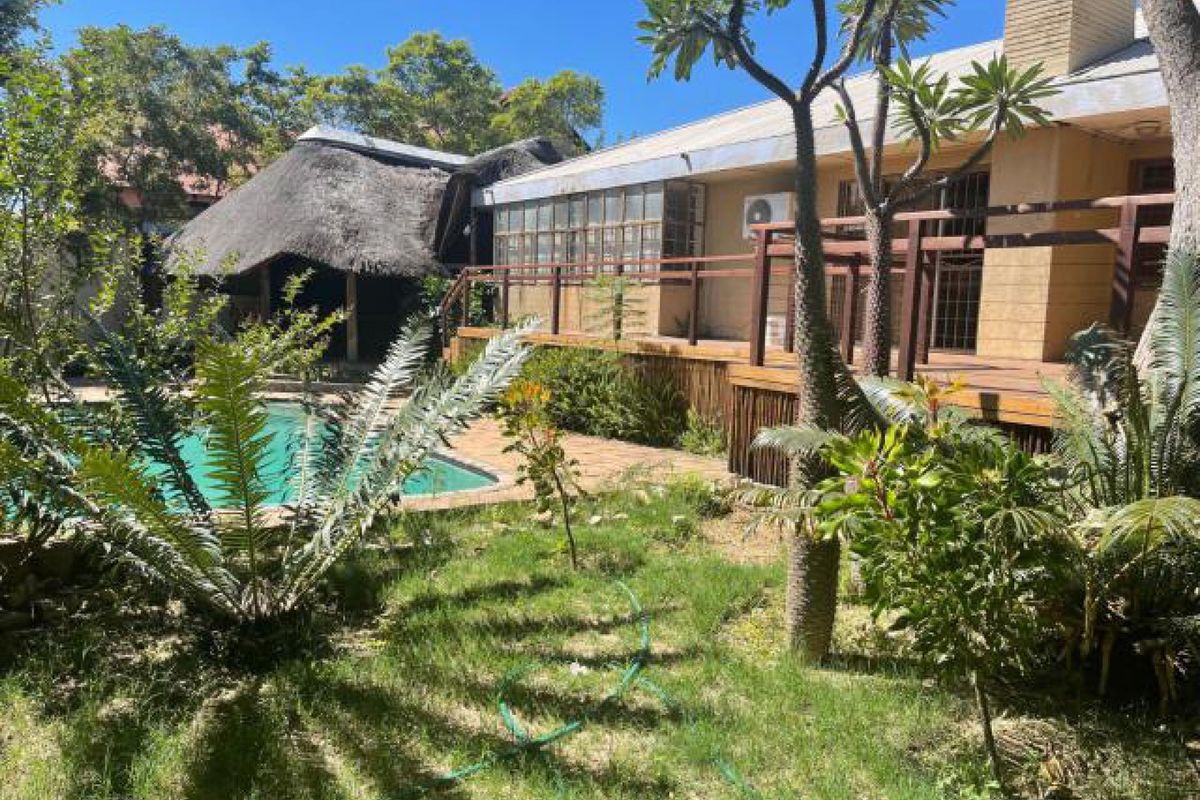 Rear garden area featuring a swimming pool, a thatched lapa, and a raised wooden deck attached to the main house structure.