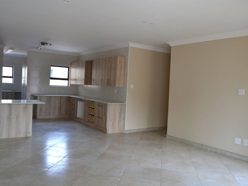 Spacious open-plan kitchen and living area featuring modern wood-finish cabinetry, stone countertops, and neutral tiled flooring throughout.