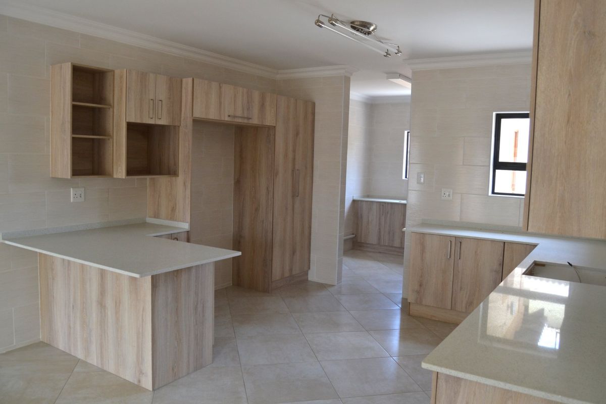 A modern, empty kitchen featuring light wood-grain cabinetry, stone countertops, a breakfast bar, and neutral tiled finishes throughout.
