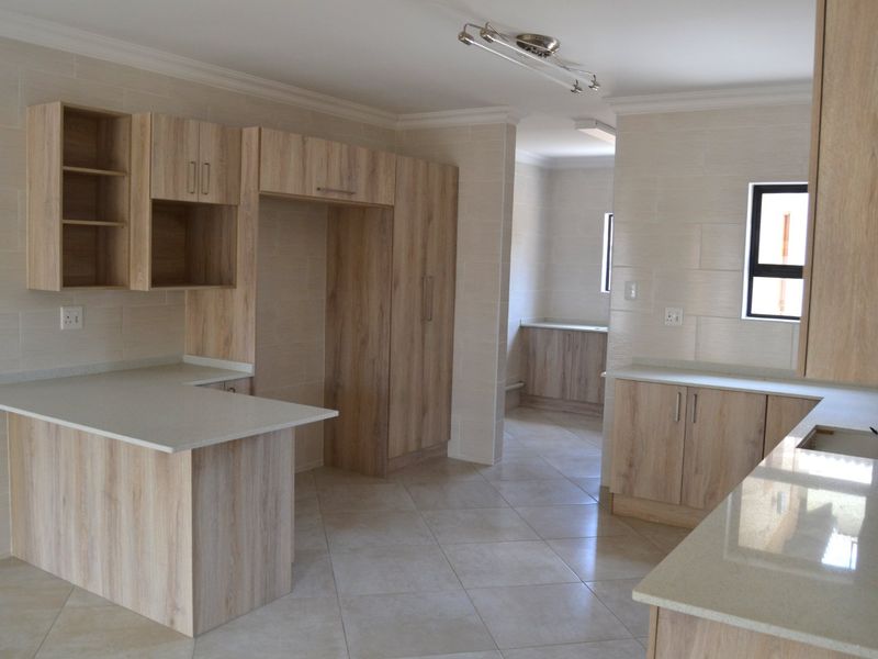 A modern, empty kitchen featuring light wood-grain cabinetry, stone countertops, a breakfast bar, and neutral tiled finishes throughout.
