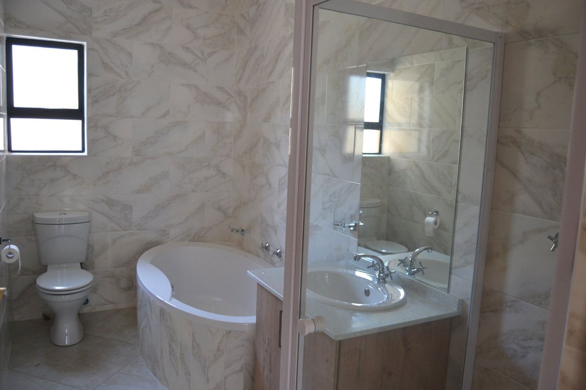 A modern bathroom featuring a built-in bathtub, vanity with basin, and floor-to-ceiling marble-look wall tiles.