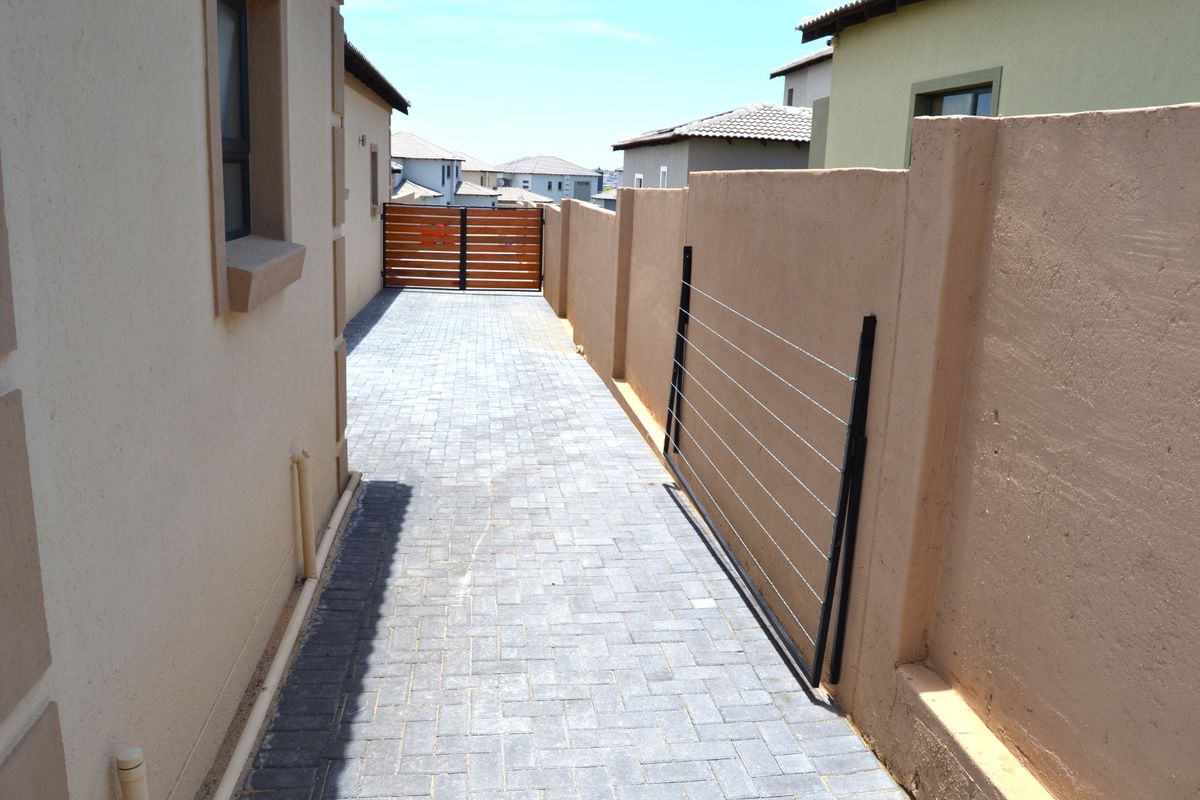 A side passage featuring paved flooring, a boundary wall, and a timber gate providing access to the rear of the property.