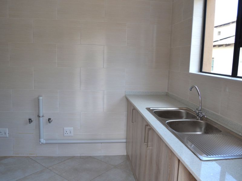 A clean, modern scullery area featuring a double bowl stainless steel sink, stone countertops, and ample cabinetry with tiled wall finishes.