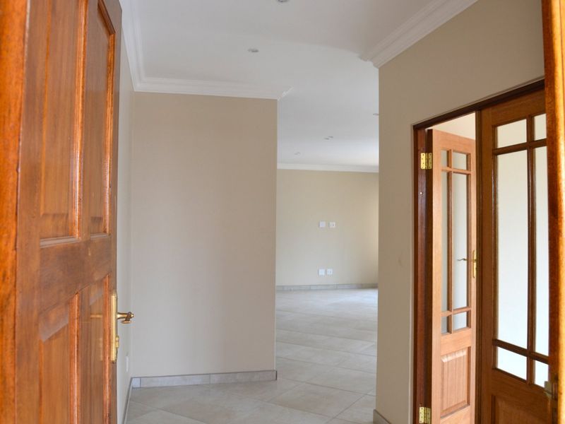 A bright and spacious hallway featuring tiled flooring, coved cornicing, and classic wooden panelled doors leading into an open living area.