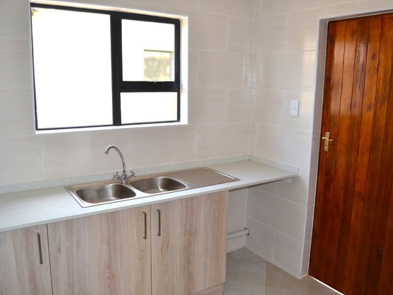 A clean and functional scullery area featuring a double bowl stainless steel sink, light wood cabinetry, and neutral wall tiling.
